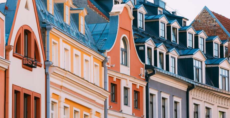 Riga, Latvia. The View Of Mansard Red Tile Roof With Four Gable Fronted Dormer Windows On The Old Building Under Blue Sky.